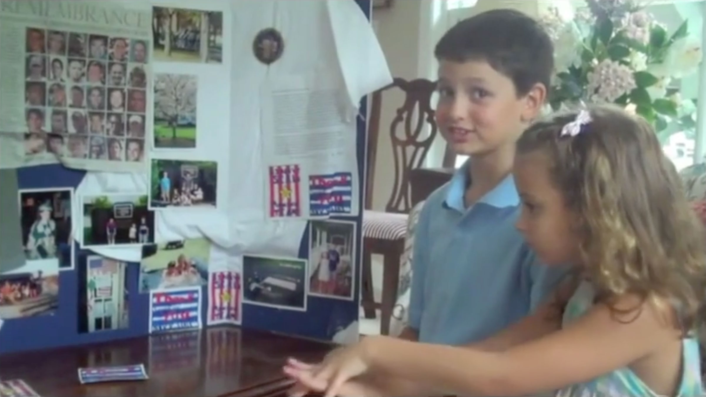 A young boy and girl stand excitedly beside a project board filled with photos and text in a cozy room. The mood is cheerful and engaging.